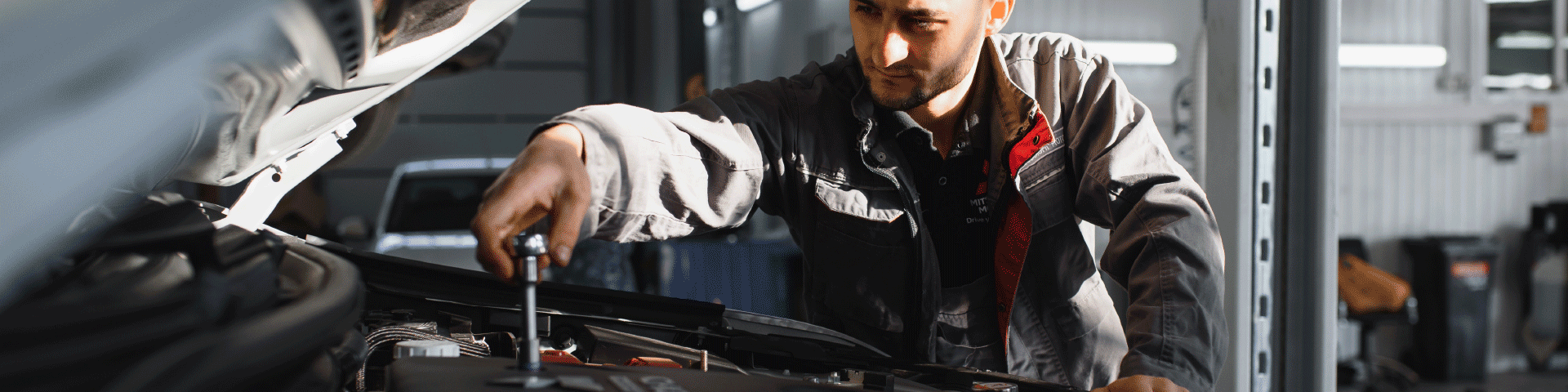 Image of a mechanic holding a wrench, working on a car’s engine.
